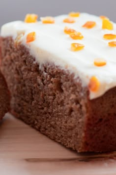 a piece of cake with white frosting and orange candies on top is sitting on a cutting board