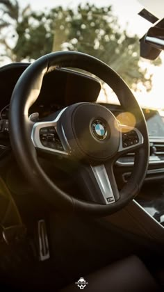 the interior of a bmw car with its steering wheel and dash lights on, in front of trees