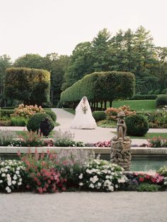 a bride and groom standing in the middle of a garden with flowers on either side