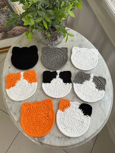 six crocheted coasters with black, white and orange cats on them sitting on a marble table