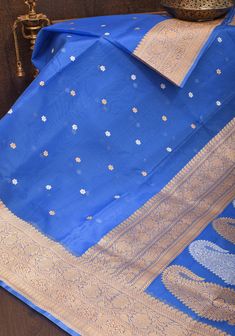 This Blue saree in pure Kora silk / Pure Organza from Banaras is adorned with gold and silver chunri butis and resplendent Elongated Paisley motifs that represent the fine craftsmanship and weaving heritage of Banaras! The Blue color serves as an amazing base for all the gold and silver zari work featured in the saree.  This drape could come to your rescue for a number of occasions from a simple family gathering to a big wedding. The fabric is sheer, mildly crisp and dreamy! SILK MARK CERTIFIED This saree is ready to wear with fall and pico done. Handmade silk tassels adorn the pallu and add more grace to it. An unstitched blouse fabric is included. *Note: There may be minor variations in the shade, the texture of the product. Hues/textures show differently due to variations in screen sett Blue Paithani Silk Dupatta With Traditional Patterns, Kora Silk Sarees, Paisley Motifs, Silk Tassels, Blue Saree, Saree Blouses, Zari Work, Of Sarees, Big Wedding