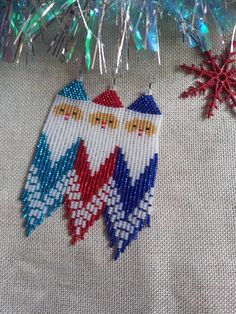 two cross stitch christmas ornaments hanging from a tree branch with tinsel and red white and blue decorations