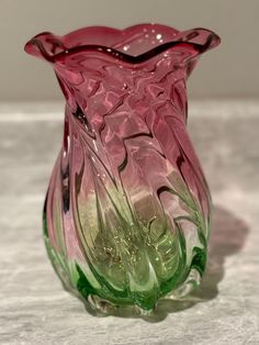 a pink and green glass vase sitting on top of a table next to a white wall