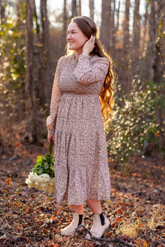 girl standing in a forest with a pink floral dress and white roses Modest Midi-length Smocked Dress With Floral Print, Modest Smocked Dress For Spring Garden Party, Spring Garden Party Prairie Dress With Smocked Bodice, Modest Fitted Smocked Dress For Garden Party, Modest Midi Dress With Smocked Cuffs, Modest Midi Dress With Smocked Back For Garden Party, Garden Party Midi Smocked Dress With Ditsy Floral Print, Cottagecore Midi Dress With Smocked Bodice, Mid-length Midi Dress For Fall Garden Party