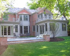 a large brick house with an attached deck and patio in the front yard, surrounded by lush green grass