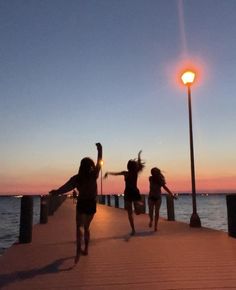 three girls are running along the pier at sunset