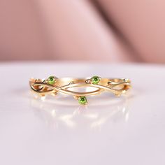 a gold ring with two green stones on it's sides, sitting on a white surface