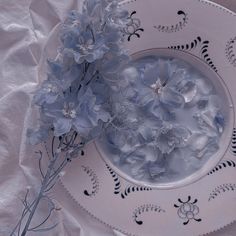 some blue flowers are in a white bowl on a table cloth with an empty plate