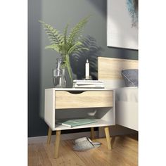 a white nightstand with a plant on top of it next to a bed in a room