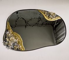 a mirror with gold and black designs on the bottom, sitting on a white surface