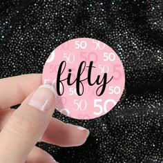 a woman's hand holding a pink sticker with the word fifty printed on it