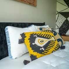 a yellow and black pillow sitting on top of a white bed next to a wooden headboard