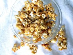 a bowl filled with popcorn sitting on top of a white table cloth next to a glass container