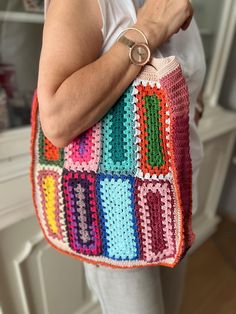 a woman holding a multicolored crocheted bag