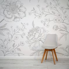 a white chair sitting in front of a wall with flowers painted on the wall behind it