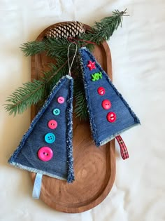 two christmas trees made out of old jeans and buttons on a wooden platter with pine cones