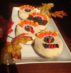 three cupcakes decorated like turkeys on a white plate with autumn leaves around them