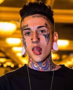 a young man with tattoos on his face and tongue sticking out from under his nose