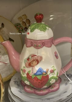 a tea pot with a strawberry on it sitting on top of a plate next to other plates