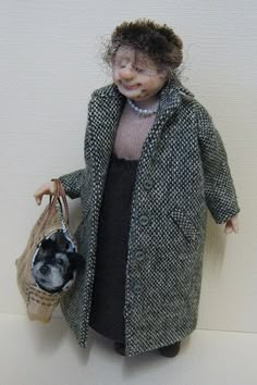 a doll is holding a basket with a dog in it's lap and wearing a coat