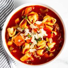 a white bowl filled with pasta and meat soup on top of a striped napkin next to a spoon