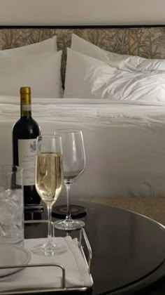 two glasses of wine on a table in front of a bed