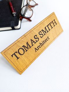 a wooden name tag sitting on top of a table next to glasses and a pen