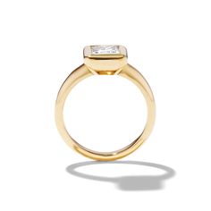 a yellow gold ring with a princess cut diamond set in the center, on a white background