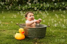 a baby sitting in a metal tub with soap bubbles floating around him and an orange rubber duck