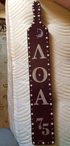 a close up of a wooden sign on a white cloth covered chair with beads and pearls