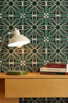 a desk with a lamp and books on it next to a wallpapered background