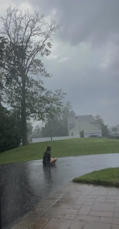 a person sitting on the ground in the rain with an umbrella over their head,