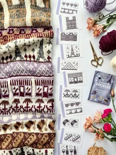 some knitting supplies are laid out on a table next to yarn and scissors, along with flowers