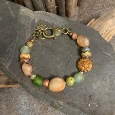 "Summertime" - The bracelet features peach silver coated quartz gemstone that glimmer like the hot sky of a late summer afternoon.  The deep greens of African glass and agate rounds are reminiscent of the thick park grass with the wavey floral discs being the prolific perennial summer flowers with the rust colored Dahlia coin as the grand centerpiecre of the gardens. A large jade nugget pulls the landscape together.  A beautiful bronze heart lobster claw closure completes the summertime cirlce.  As Ella Fitzgerald sings while Louis Armstrong trumpets, "Summertime, and the living is easy". Grab a pcinic basket, a blanket and a good book and look will be complete. Size 7.50. I can adjust this to fit up to to 8.5 inches.  Please let me know your desired size. I begin each piece by hand select Earthy Orange Jewelry As Gift, Handmade Bohemian Glass Beaded Bracelets, Adjustable Vintage Bracelets For Summer, Adjustable Orange Beaded Bracelets With Natural Stones, Bohemian Adjustable Glass Jewelry, Adjustable Bohemian Glass Jewelry, Orange Bohemian Jewelry For Summer, Bohemian Orange Jewelry For Summer, Bohemian Style Adjustable Glass Jewelry