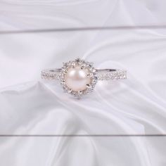 a white pearl and diamond ring sitting on top of a white cloth