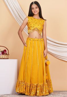 Faux Georgette Lehenga in Mustard This Readymade Round Neck and Sleeveless attire with Cotton Lining is Enhanced with Dangles, Resham, Sequins and Gota Lace Work Available with a Faux Georgette Choli in Mustard, a Matching Potli Bag and an Organza Dupatta in Marble Dyed Shaded Yellow Do note: (1.)Accessories shown in the image is for presentation purposes only. (2.)Half to one inch may vary in measurement. (3.)Slight variation in actual color vs. image is possible. We sell all kinds of Kidswear. Sleeveless Party Set For Navratri, Embellished Sleeveless Sets For Festivals, Embellished Sleeveless Festival Sets, Yellow Anarkali Set With Sequins, Bollywood Style Sleeveless Party Sets, Traditional Sleeveless Party Sets, Sleeveless Sets For Party Festivals, Sleeveless Sets For Party And Festivals, Sleeveless Party Sets For Festivals