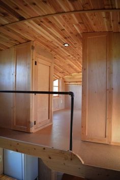 an empty room with wood paneling and metal railings on the floor, looking into the kitchen