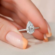 a woman's hand holding an engagement ring with a pear shaped diamond on it