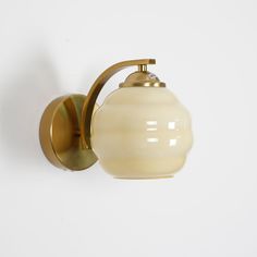 a wall light with a white glass shade on it's arm and a brass finish