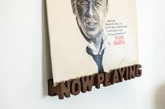 a wooden sign that reads now playing with a man's face on the wall