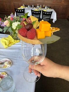 a person is holding a wine glass with cheese and raspberries on the table