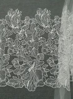 a white lace with flowers on it sitting next to a piece of sheer fabric in front of a black background