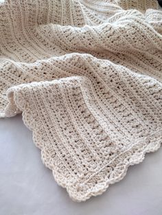 a white crocheted blanket laying on top of a bed next to a pillow