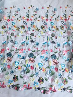 a white table cloth with colorful flowers and butterflies on it, sitting on top of a bed