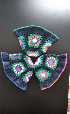 three pieces of crochet are sitting on a black surface, one is blue and the other is multicolored