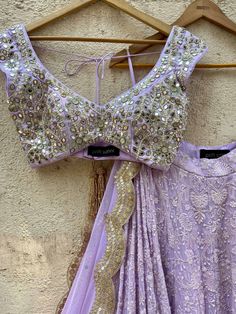 A three-piece lavender lucknowi mirror lehenga set from the Priti Sahni collection. This elegant lavender georgette lehenga with heavy gota, sequins, pearl and zari work border is paired with lavender blouse in raw silk fabric with mirror, pearl and zardozi hand work embroidery. The lehenga has side hanging ball tassels to the waistline. And the blouse has a sequins tassel tie-up at the back. The outfit is completed with a lavender mirror net dupatta with scalloped edging. Anarkali Lavender Sharara For Reception, Lavender Sharara With Zari Work For Festivals, Festival Lavender Sharara With Zari Work, Lavender Bollywood Sharara With Zari Work, Festive Lavender Sharara With Zari Work, Elegant Designer Lavender Lehenga, Elegant Lavender Designer Lehenga, Bollywood Style Lavender Sharara With Zari Work, Lavender Choli With Dupatta For Reception