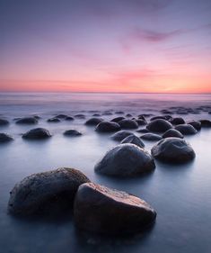 several large rocks sitting on top of a beach next to the ocean at sunset or dawn