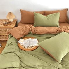 a bed with green sheets and pillows on top of it next to a wicker basket