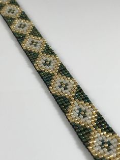 a close up of a bracelet on a white surface with gold and green beads in the middle