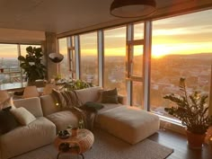 a living room filled with furniture and large windows overlooking the city at sunset or dawn